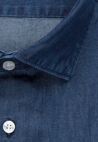 Denimblauer Hemdkragen mit Doppelnähten und zwei weißen Knöpfen, die die Stoffstruktur und die Knopflochansicht in Nahaufnahme zeigen.