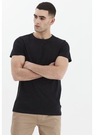 Fekete pamut póló kerek nyakkal és rövid ujjakkal, laza szabással és sima textúrával. A modellen khaki nadrág van.