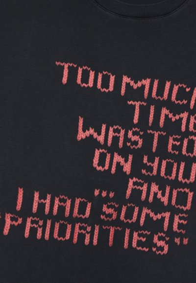 Sort bomulds T-shirt med stor, pixelagtig rød tekst med sætninger, der skaber et kontrasterende design. Blød tekstur og rund halsudskæring.