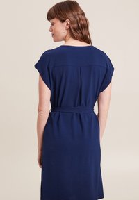 Navyblaues Kurzarmkleid mit einem Taillengürtel, strukturiertem Stoff und einer lockeren Passform mit einem mittellangen Saum. Minimalistisches Design.