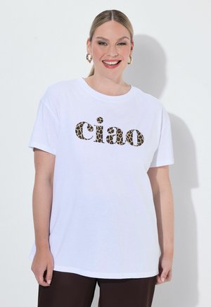 Lachende vrouw met licht haar in een staart draagt een wit T-shirt met "ciao" in luipaardprint en gouden creolen tegen een effen achtergrond.