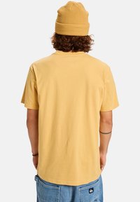 Žluté bavlněné tričko s krátkým rukávem, s kulatým výstřihem a volným střihem. Spárováno s odpovídající žlutou pletenou čepicí.