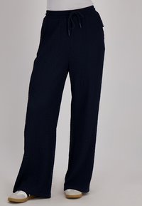 Marineblauwe wijde broek met een textuurstof, een elastische tailleband en een trekkoorddetail. Casual pasvorm met een rechte snit tot op de vloer.