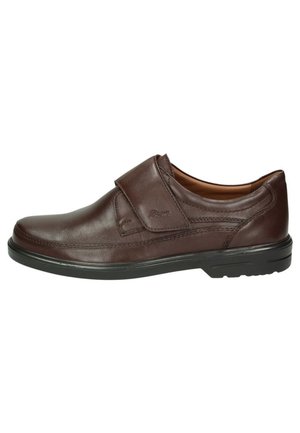 Brauner Lederschuh mit Klettverschluss, runder Zehenform und kontrastierender schwarzer Gummisohle. Glatte Textur und minimalistisches Design.