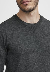 Maglione grigio lavorato a maglia con un classico scollo a girocollo, dettagli testurizzati sulle spalle e tessuto liscio e fine.
