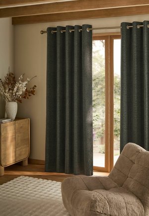 Tende grigio scuro appese a un'asta che coprono una porta di vetro con cornice in legno, con una poltrona beige in peluche e un mobile di legno con un vaso vicino.