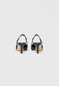 Mustat korkokengät, joissa on tyylikäs muotoilu, avoin takaosa, ohuet nilkkaremmit ja pinnaltaan teksturoitu ylämateriaali.