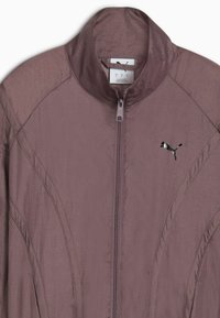 Paarse lichtgewicht jas met een hoge kraag, volledige ritssluiting en details aan de zijkant. Heeft een klein zwart logo op de borst.