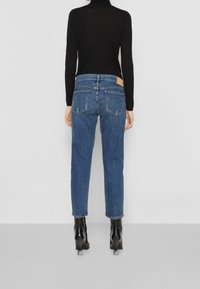 Blå denimjeans med rak passform, medelhög midja och markerade bakfickor, kombinerat med en svart långärmad topp och svarta klackstövlar.