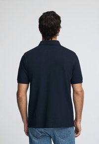 Marinblå pikétröja med korta ärmar och klassisk krage, tillverkad av texturerad bomull; bärs med ljusblå jeans och visar en enkel, avslappnad passform.