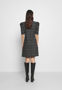 Vestido a cuadros en blanco y negro con mangas abullonadas, un corpiño ajustado y una falda acampanada, combinado con botas de tacón negras hasta la rodilla.