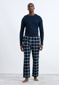 Mornarska majica dugih rukava u kombinaciji s crno-bijelim kariranim hlačama za opuštanje, koje imaju struk s podešavanjem i mekani materijal.