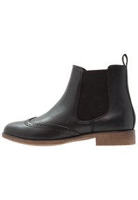 Stivaletti neri in pelle con pannelli elastici sui lati, punta rotonda, dettagli brogue e tacco basso impilato. Finitura liscia, design classico.