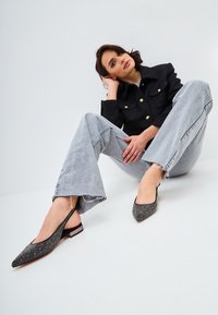 Pantofi slingback negri cu vârfuri ascuțite, ornamentați cu cuie metalice și un toc mic. Purtați cu blugi gri deschis, cu croi larg.