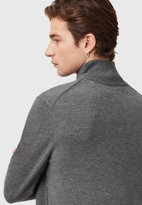 Grauer Strickpullover mit hohem Kragen und subtiler Textur, der eine taillierte Passform hat und minimale Details auf der Rückseite aufweist.