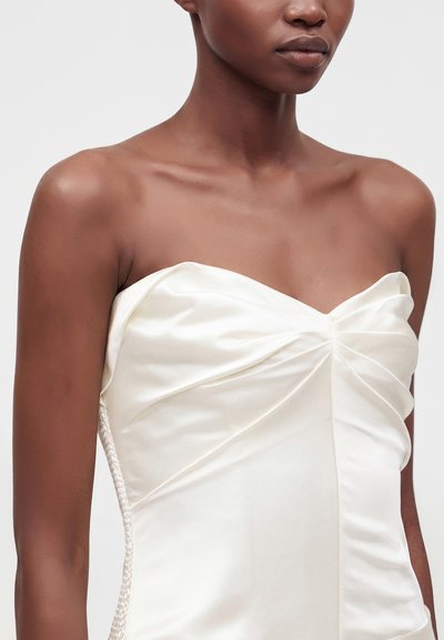 Gros plan d'une personne portant une robe bustier en satin blanc avec un léger froncé au niveau de la poitrine et un corsage lisse et ajusté.