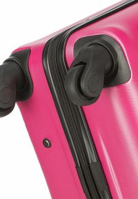 Pink hard-shell suitcase with a textured surface, black zipper, and dual rotating wheels for mobility. Features a side handle and security latch.