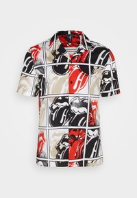 Camisa de manga corta con un patrón gráfico multicolor en rojo, negro, beige y blanco, con labios llamativos y un diseño cuadrado.