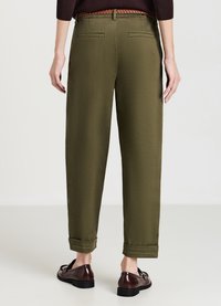 Pantaloni verdi con vita elastica, gamba dritta, orli a risvolto e due tasche posteriori. Abbinati a mocassini marroni per un look informale.