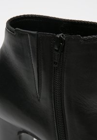 Gros plan sur une botte de cheville en cuir noir avec une fermeture éclair sur le côté et un bord tressé le long de l'ouverture.