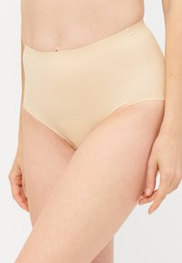 Beige hooggeld briefs gemaakt van glad, rekbaar materiaal, met een naadloos ontwerp zonder zichtbare naden of sluitingen.