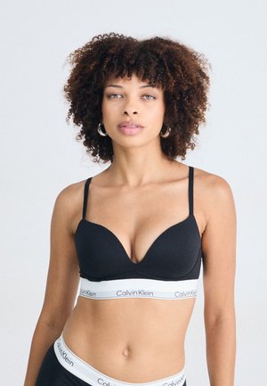 Zwarte push-up bh met dunne verstelbare schouderbanden, voorzien van een witte Calvin Klein band. Gladde stof, minimalistisch ontwerp en voorgevormde cups.