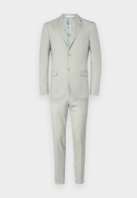 Šviesiai pilkas kostiumas su viena skyle, dviem mygtukais, notch tipo apykakle ir atitinkančiomis siaurėjančiomis kelnėmis. Lygus tekstūra, minimalūs detalės.