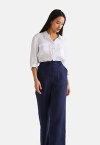 Chemise en lin blanche à boutons avec deux poches poitrine, associée à un pantalon large en lin bleu marine doté d'une taille à cordon de serrage et de poches latérales.