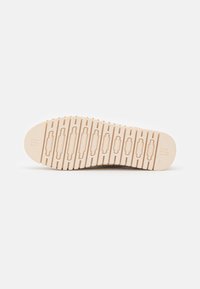 Suola di sneaker beige chiaro con scanalature orizzontali e dettagli, caratterizzata da un motivo testurizzato e un logo del marchio in rilievo sulla punta.