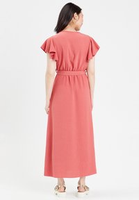 Robe maxi en tissu corail, dotée de manches courtes à volants, d'une taille cintrée et d'une jupe fluide. Texture lisse avec une sensation légère.