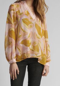 Genomskinlig, lätt blus i rosa och gult med blommigt mönster. Har V-ringning, långa ärmar och rosa knäppte manschetter. Texturerad tyg.