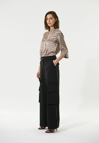 Seidenbluse mit geometrischem Muster in Beige und Braun, kombiniert mit schwarzen weit geschnittenen Cargo-Hosen mit mehreren Taschen und seitlichen Schlitzen.