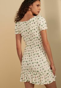 Robe blanche avec imprimé floral vert et rose, corsage smocké, manches bouffantes courtes et ourlet froncé. Fabriquée en tissu léger et texturé.