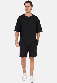 Zwart katoenen oversized T-shirt met korte mouwen gecombineerd met zwarte shorts. Witte sneakers maken de outfit compleet. Simpel, casual ontwerp.