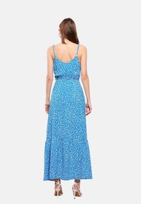 Blauwe bloemenmaxi-jurk met dunne spaghettibandjes en een gelaagde zoom. Het materiaal is zacht met een gladde textuur en een getailleerde taille.