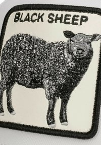 Schwarzes Schaf-Patch mit schwarzem besticktem Schaf-Design auf weißem Hintergrund. Eingefasst von einem schwarzen Rand, mit strukturiertem Woll-Detail.