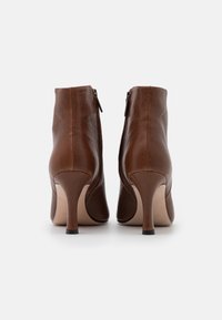 Brune læderankelstøvler med et elegant design, spids snude og 4-tommer stiletthæl. Har en lynlås i siden for nem påtagning.