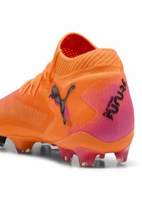 Le scarpe da calcio Puma presentano una parte superiore arancione brillante con un design in gradiente rosa, una superficie testurizzata e il logo Puma nero sul lato.