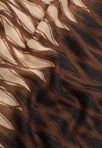 Tissu marron à motifs avec des vagues crème et des accents foncés, présentant une texture douce avec une finition lisse. Idéal pour diverses utilisations textiles.