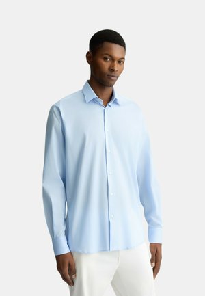 Camicia a maniche lunghe azzurro chiaro realizzata in tessuto liscio. Presenta un colletto appuntito e chiusura con bottoni. Vestibilità elegante con orlo curvo.
