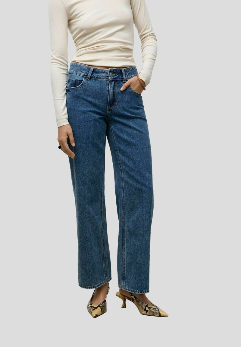 Heledasinine, kõrge vöökohaga laiad teksapüksid klassikalise denimitekstuuriga, millele on sobitatud mustriga beežid ja mustad kontsakingad.