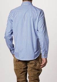 Camisa de manga larga a cuadros en azul y blanco, de tela de algodón, vista trasera con puños abotonados y dobladillo curvado. Pantalones marrones visibles por debajo.