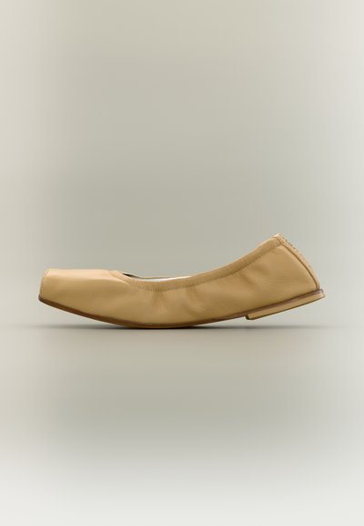 Chaussure plate en cuir beige avec un bout carré arrondi et un petit talon, présentée de profil sur un fond neutre.