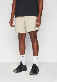 Beige athletic shorts with black Nike logo, paired with black sneakers featuring gold accents, and white socks with black logo.