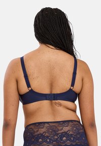 Marineblauwe bh met verstelbare bandjes en haak-en-oogsluiting. Heeft een gladde textuur met kantaccenten langs de onderste rand.