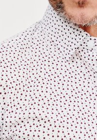 Biała koszula z wzorem małych fioletowych i niebieskich kwiatków, z kołnierzykiem zapinanym na guziki oraz teksturowanym materiałem o gładkim wykończeniu.