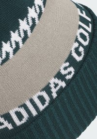 Knitted beanie featuring a dark green and beige color scheme, with "ADIDAS GOLF" text in white and a zigzag pattern along the edges.