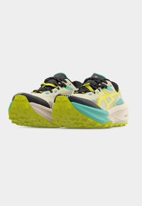 Ζευγάρι μπεζ και μαύρα παπούτσια τρεξίματος με κίτρινες λεπτομέρειες και φωτεινές πράσινες σόλες, τοποθετημένα δίπλα δίπλα και στραμμένα προς τα εμπρός.