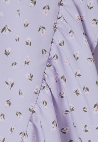 Violetti kangas kukkakuviolla, jossa on pieniä valkoisia ja vaaleanpunaisia kukkia vihreillä lehdykköillä; rypytetty pinta sauman varrella.