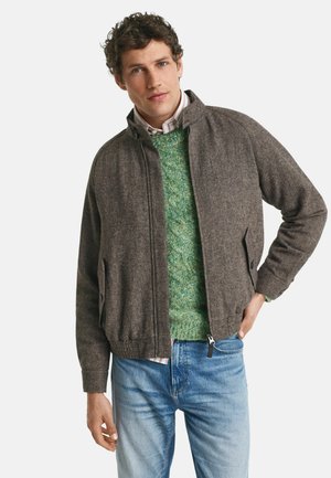 Veste zippée marron avec col montant, texture en mélange de laine, deux poches latérales, portée sur un pull vert, associée à un jean bleu.
